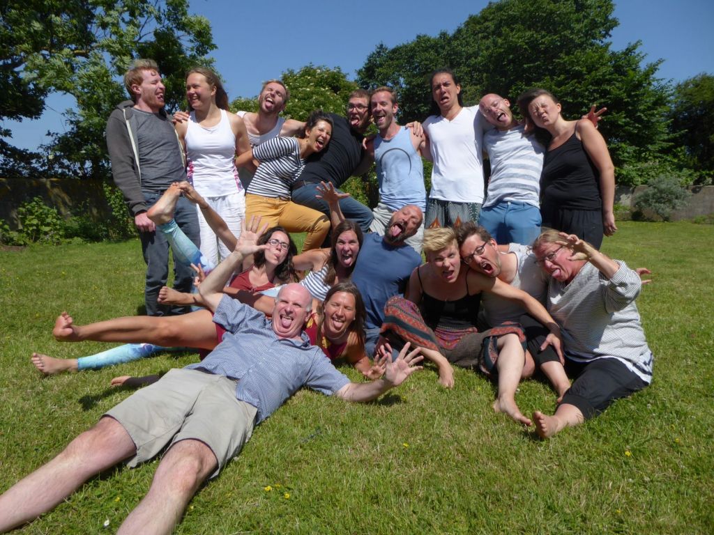 honesty europe group photo for the advanced 8 day retreat in Fehmarn Germany; 17 people standing/sitting in the grass outside making funny faces